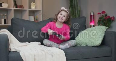 年轻的小女孩坐在沙发上在家里的客厅里播放视频。 兴奋的玩家女孩手拿操纵杆
